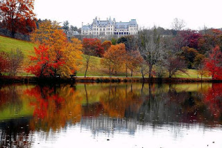 French style chateau on a hill in the fall with a large pond in front of it