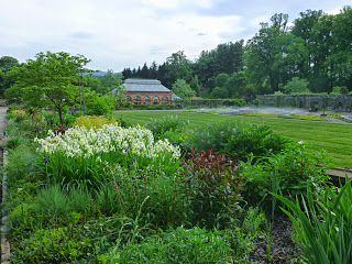 Garden full of flowers with lawn and large brick and glass building in the background