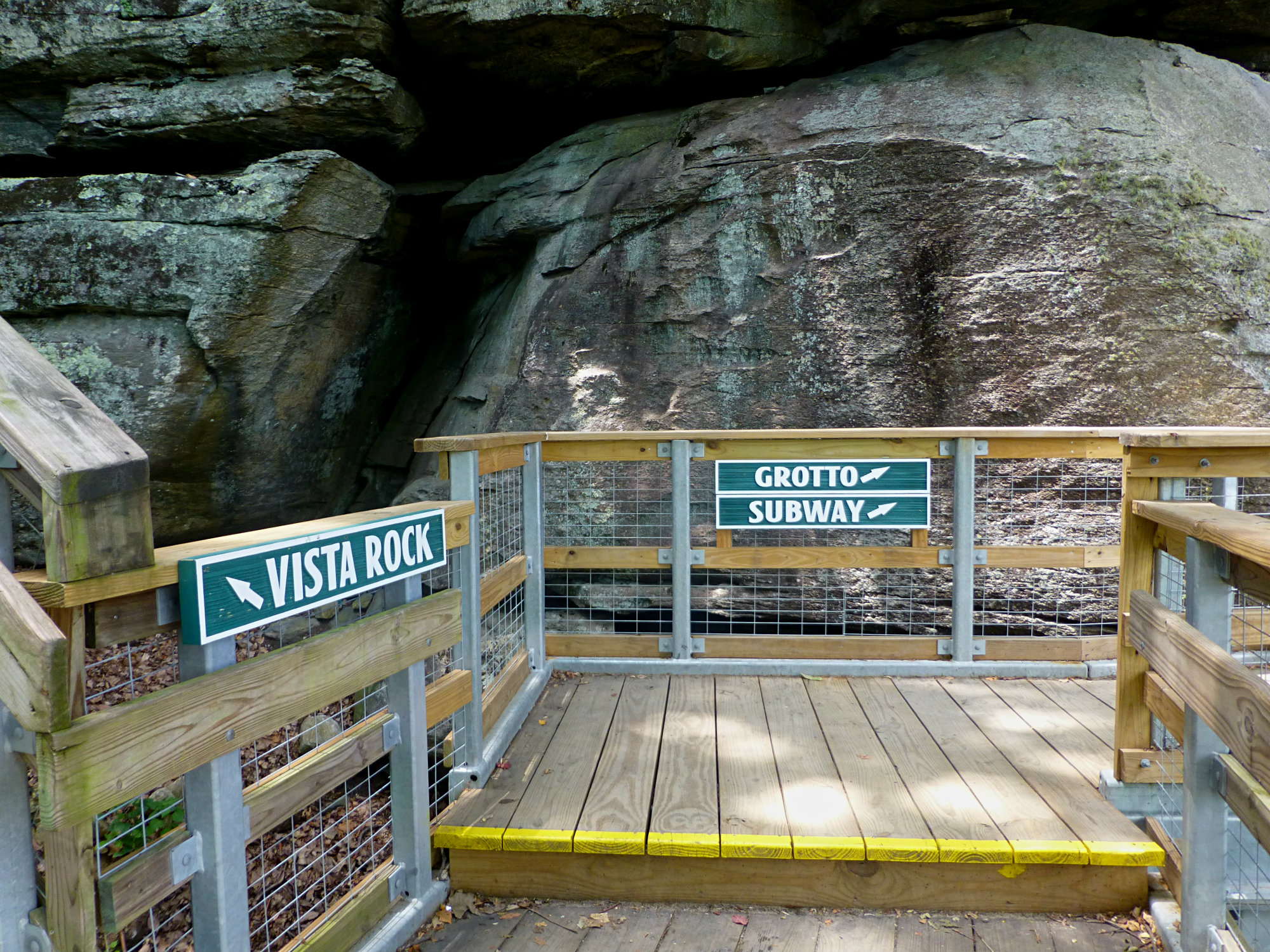Wooden boardwalk with signage leading to Grotto, Subway, and Vista Rock a boulder wall in the background