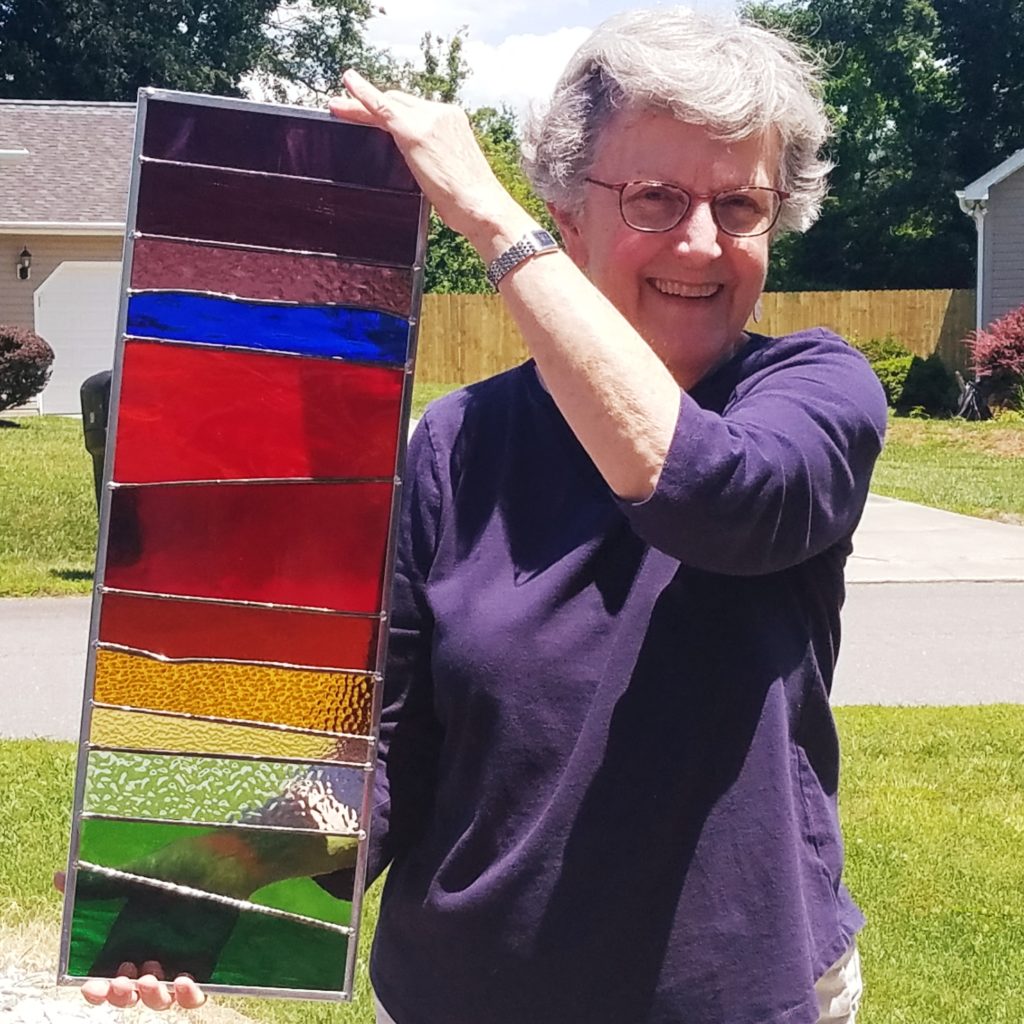 Woman smiling and holding multi-colored vertical stained glass piece of art