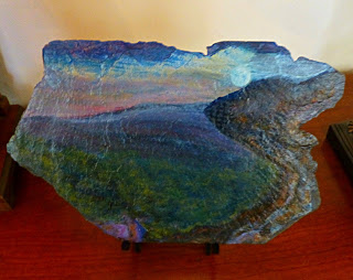 Painting on rugged slate tile of moon rising over green and blue mountain peaks