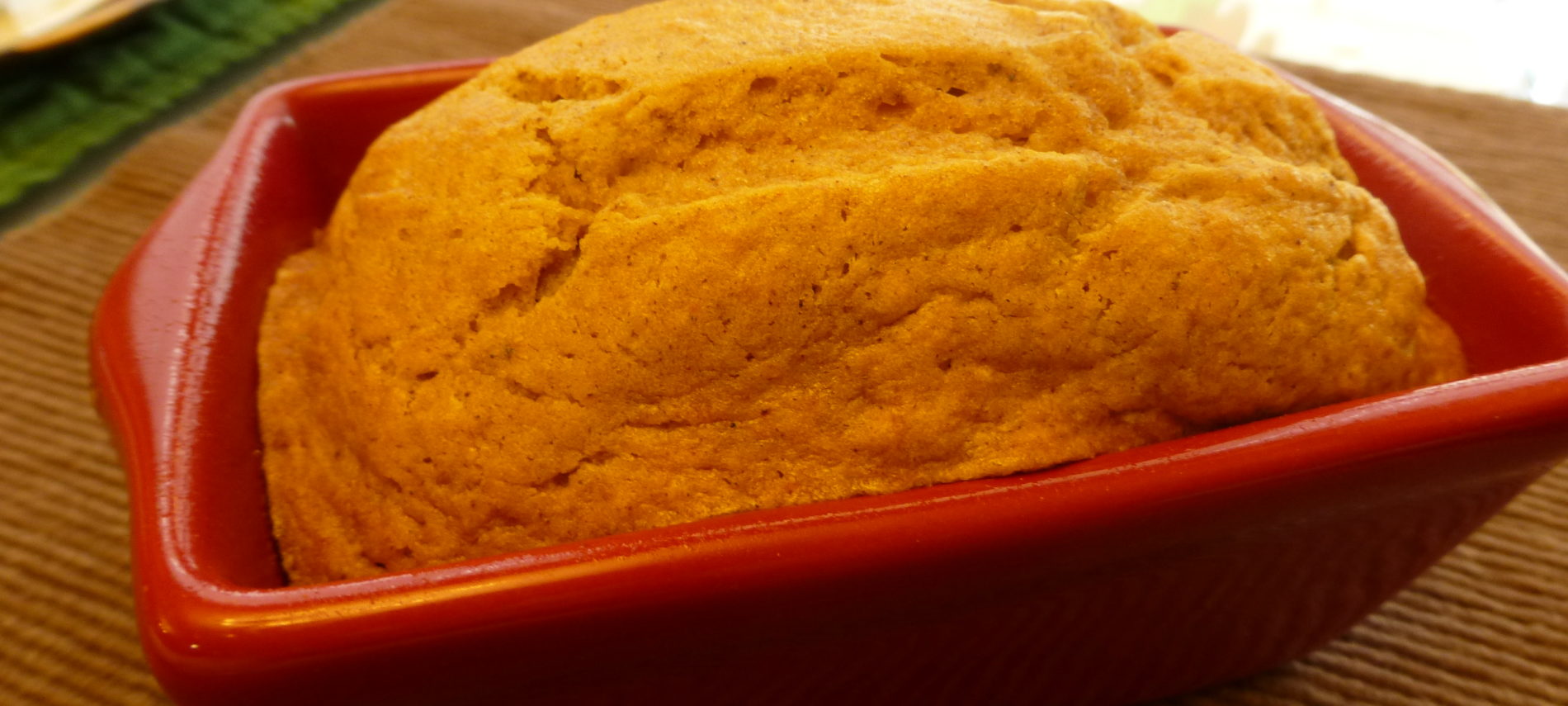 Close up of a loaf of baked bread in a ceramic loaf pan set on a placemat