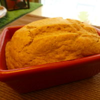 Close up of a loaf of baked bread in a ceramic loaf pan set on a placemat
