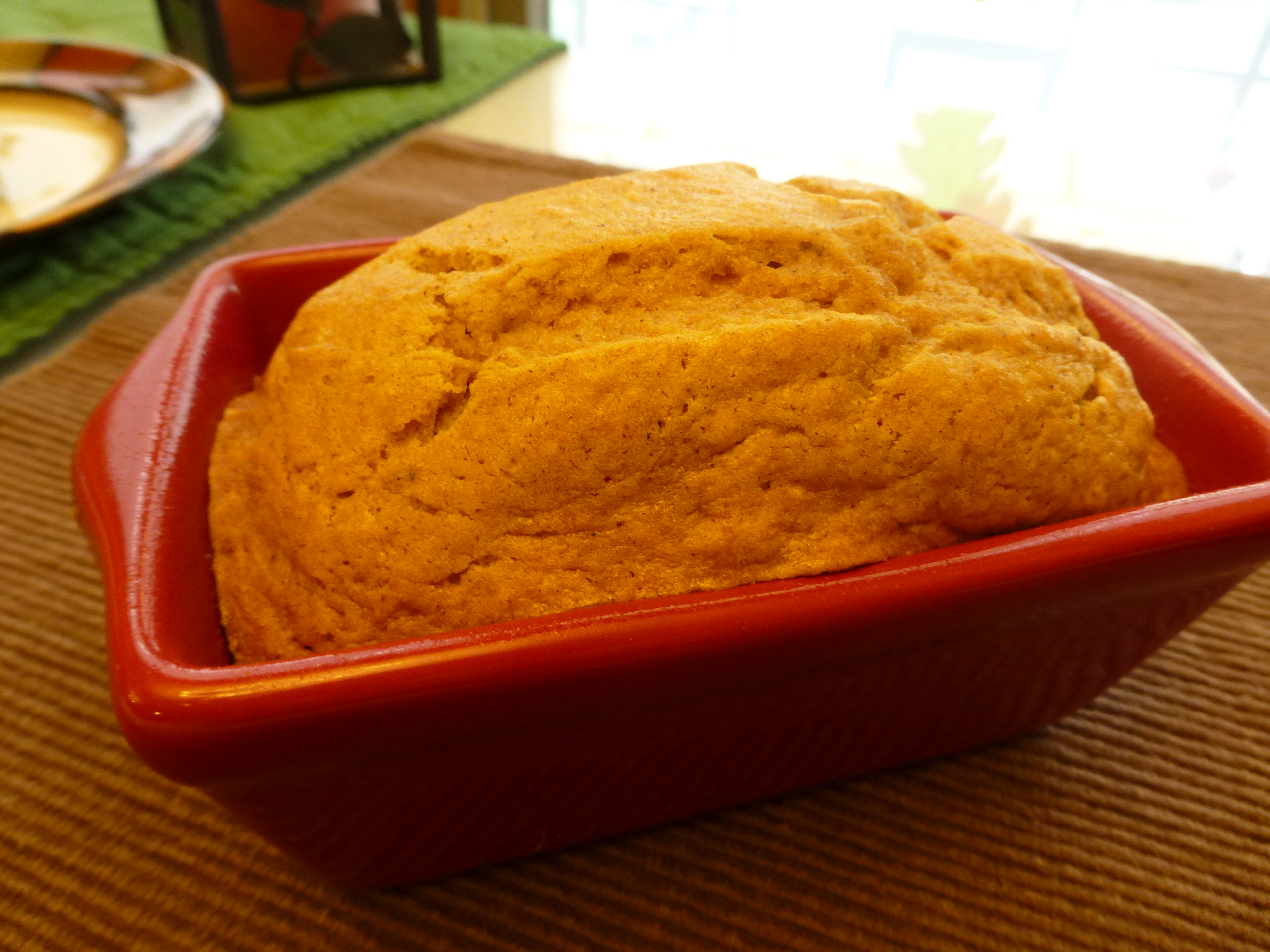 Close up of a loaf of baked bread in a ceramic loaf pan set on a placemat