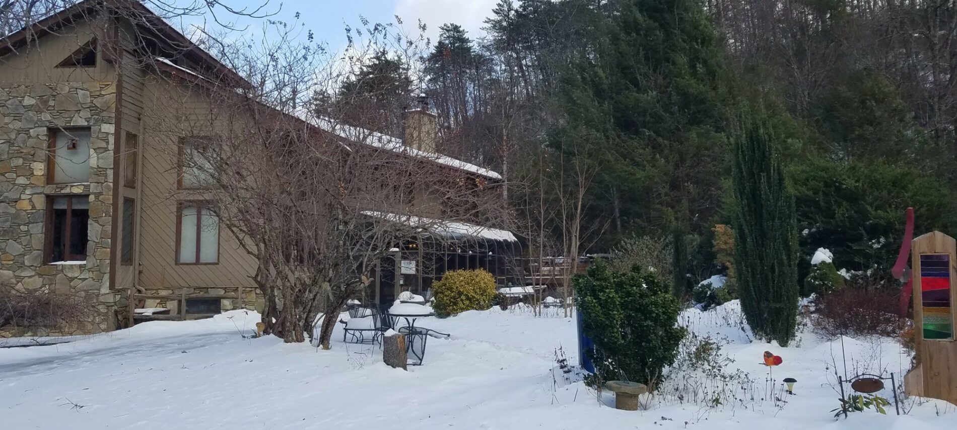 A snowy scene with a lodge style home surrounded by tall trees