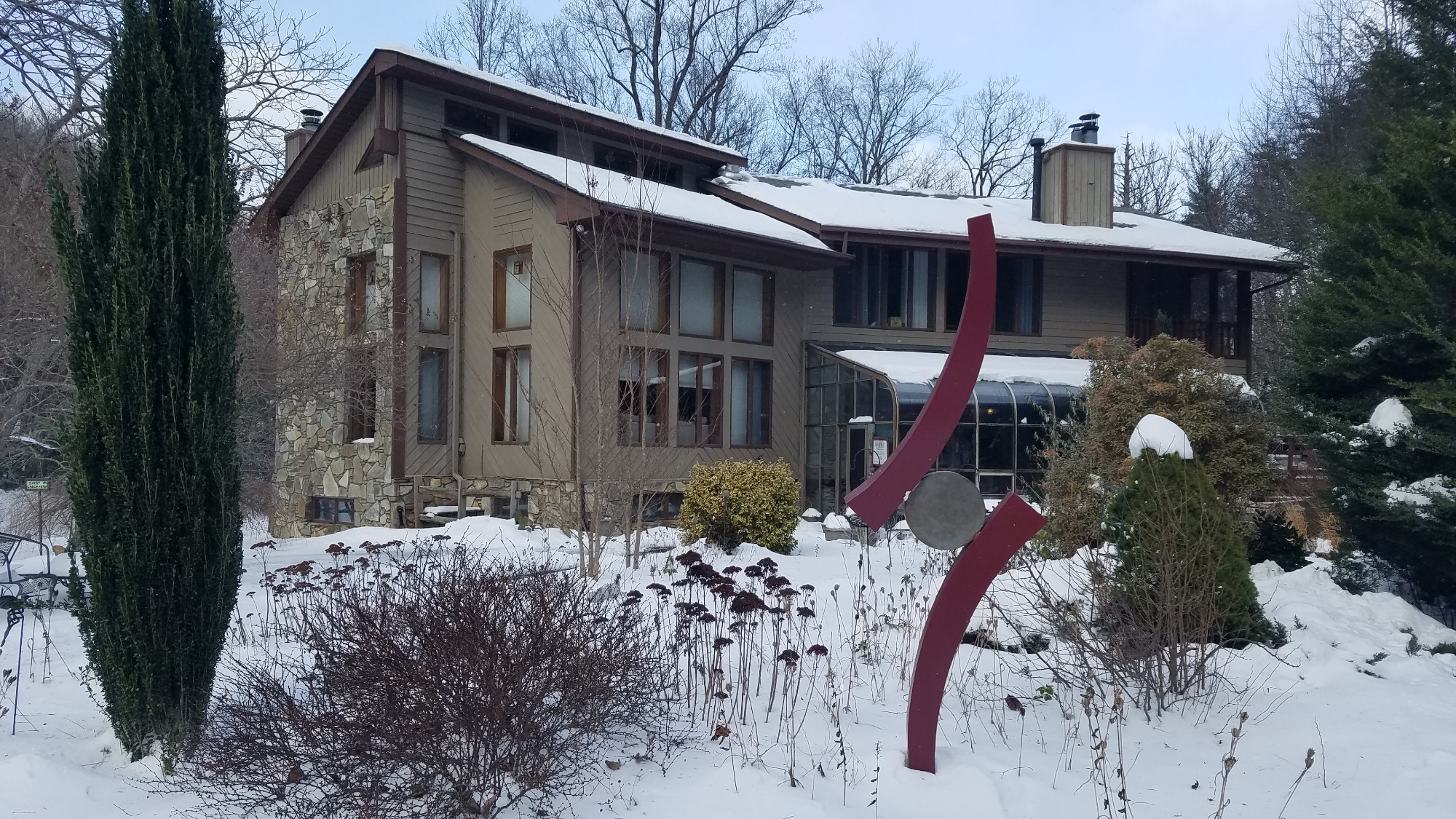 Garden sculpture with vertical curving pieces sits in the snow with lodge style home in the background