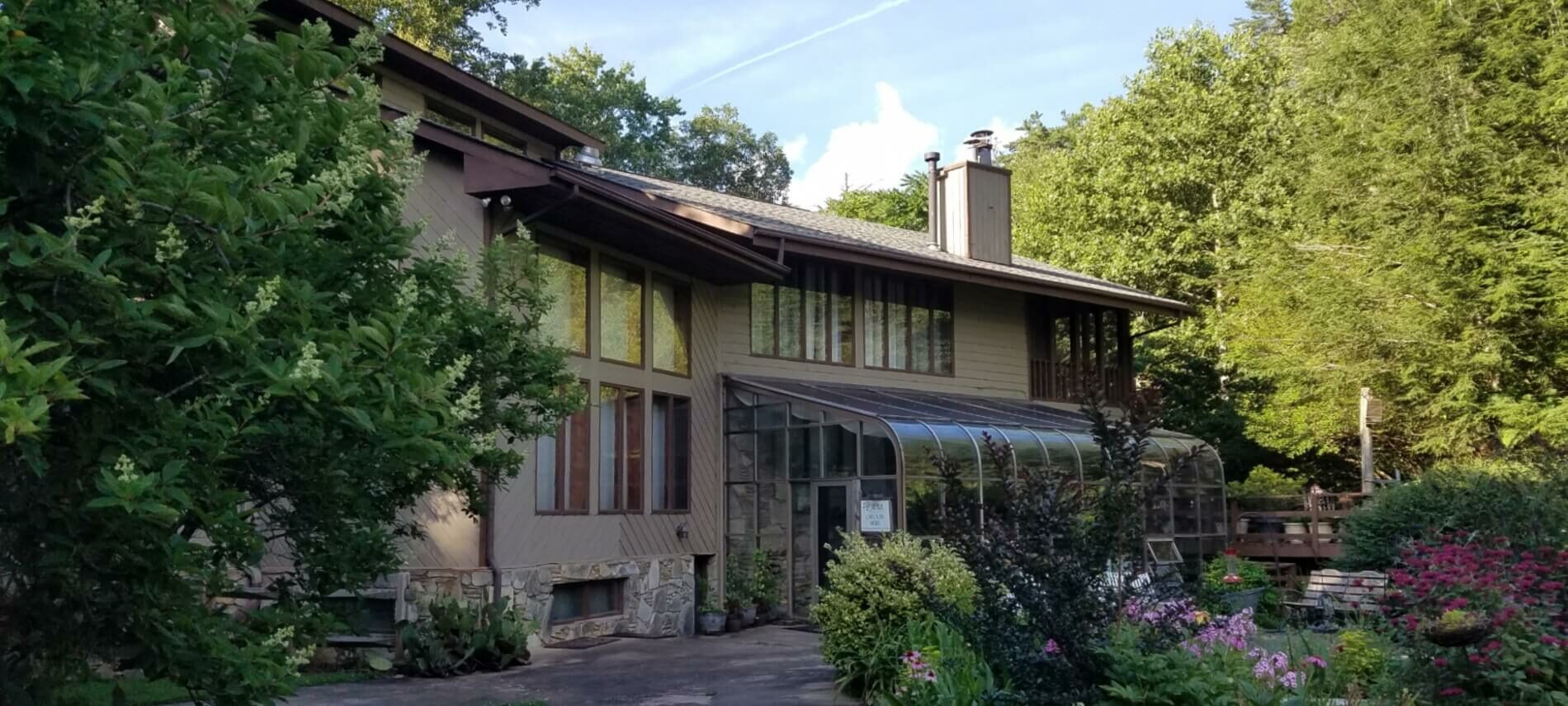 Large lodge style home with expansive windows set behind a flowering garden and surrounded by trees