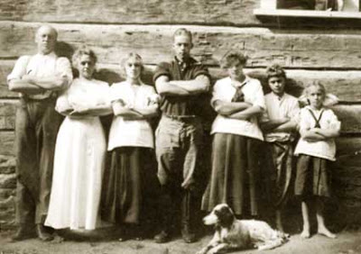 Old family photo of mother and father and five children standing in a row in front of a cabin