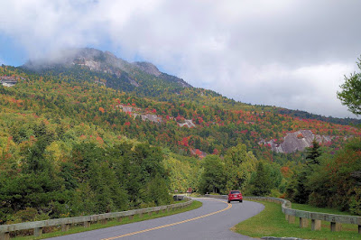 Red car on a road leading to a mountain covered in the start of fall color