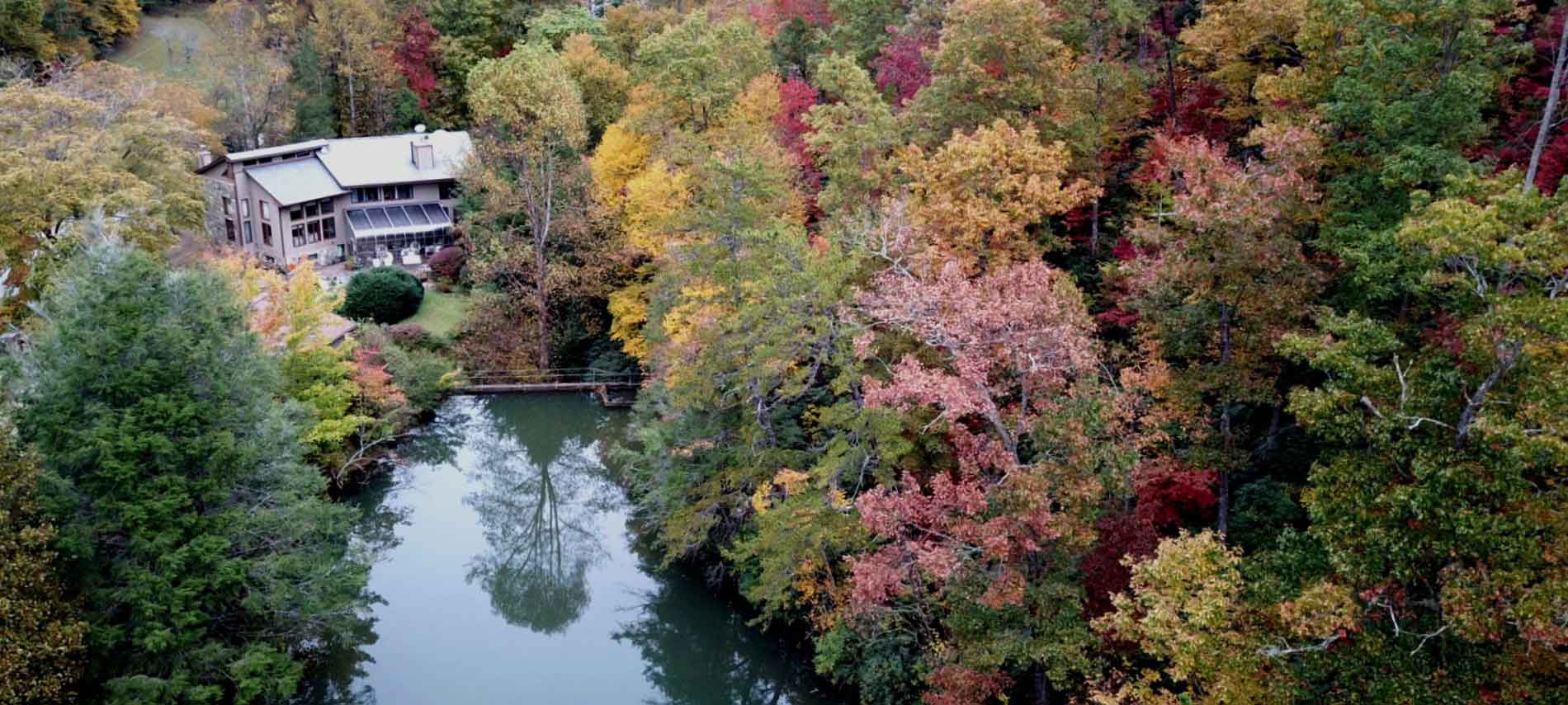 Aerial exterior view of the Inn of Mill Creek and propery including the autumn changes upon the leaves surrounding a pool of water. 