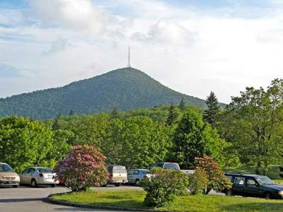 Tall mountain peak with radio tower on top and parking lot of cars in front of it