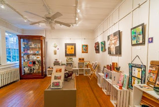 Large room with windows on one side, a display cabinet with art in it and art hanging on the walls