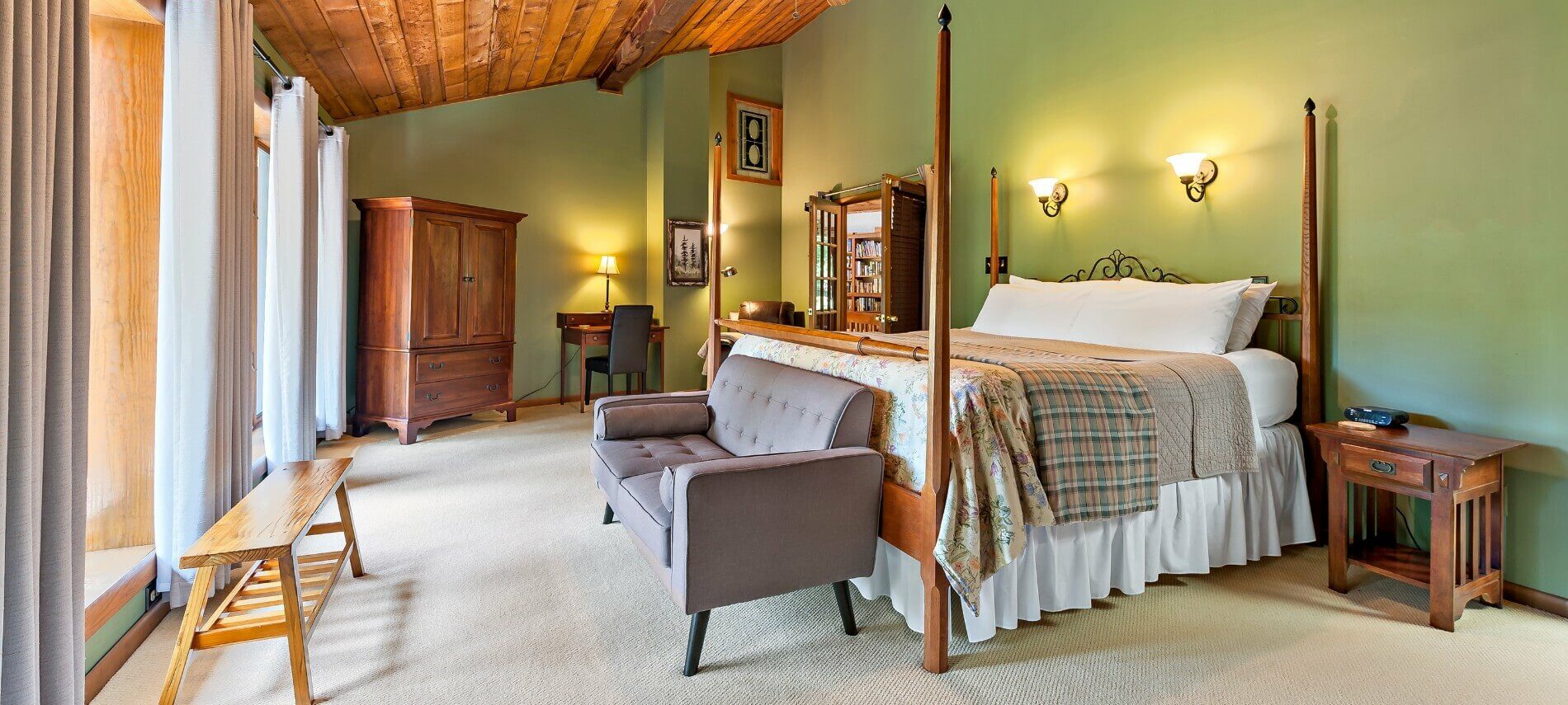 Large bedroom with vaulted cedar plank ceiling, and four poster bed facing wall of floor to ceiling windows