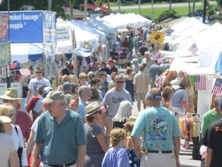 Large crowd at a street festival flanked by large white tents and concession stands