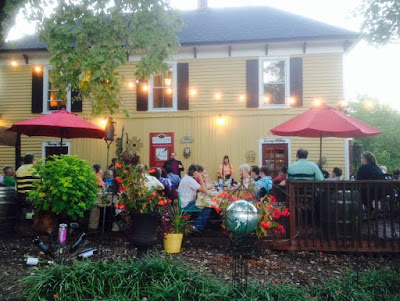 Several people sitting under red umbrellas on the deck of a yellow house